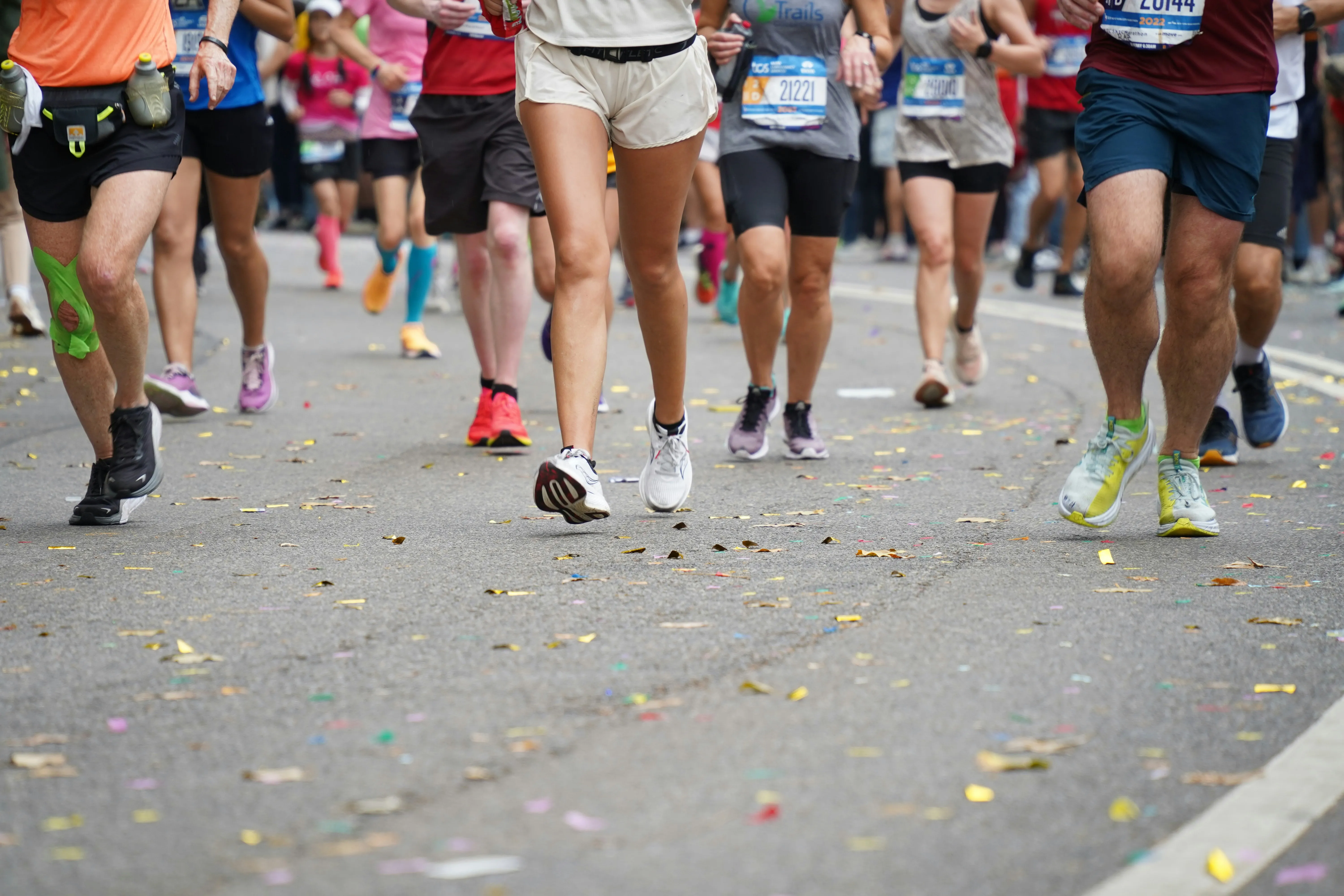 close-up van hardlopers tijdens een marathon met confetti op de weg