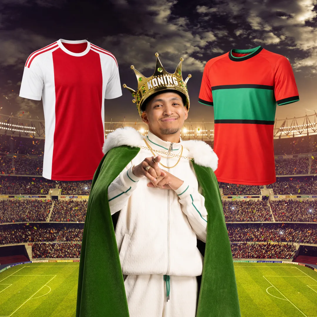 Man met koningskroon en groene mantel met voetbalshirts op achtergrond in stadion