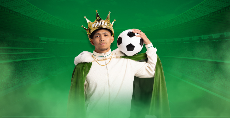 Persoon in koninklijke outfit met een voetbal (Koning TOTO), omringd door groene rook op een stadion achtergrond.