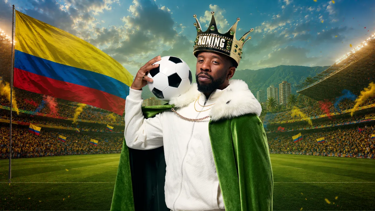 Persoon met kroon en cape houdt een voetbal vast op een stadion met Colombiaanse vlag