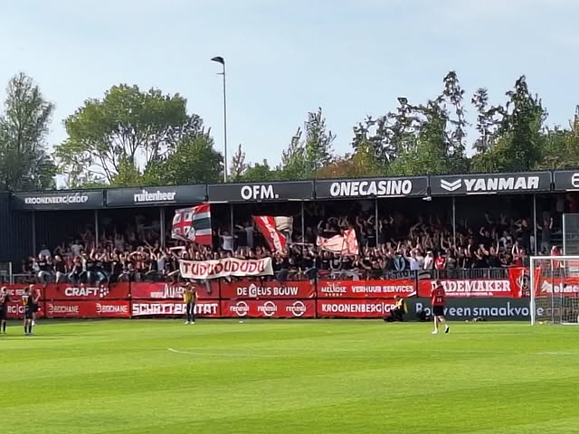 Supporters van Almere City juichen in een volle tribune met spandoeken en vlaggen achter het doel