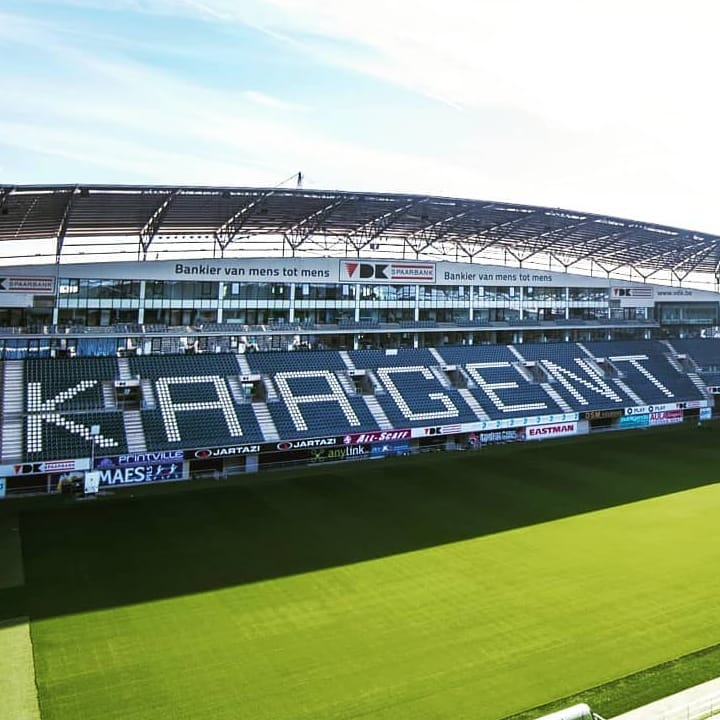 Leeg stadion van KAA Gent met tribune waarop de clubnaam in witte stoelen is weergegeven