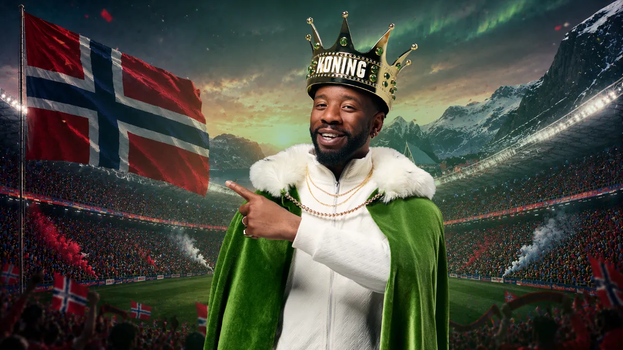Persoon met groene koningsmantel en kroon wijst naar de vlag van Noorwegen in een stadion met publiek