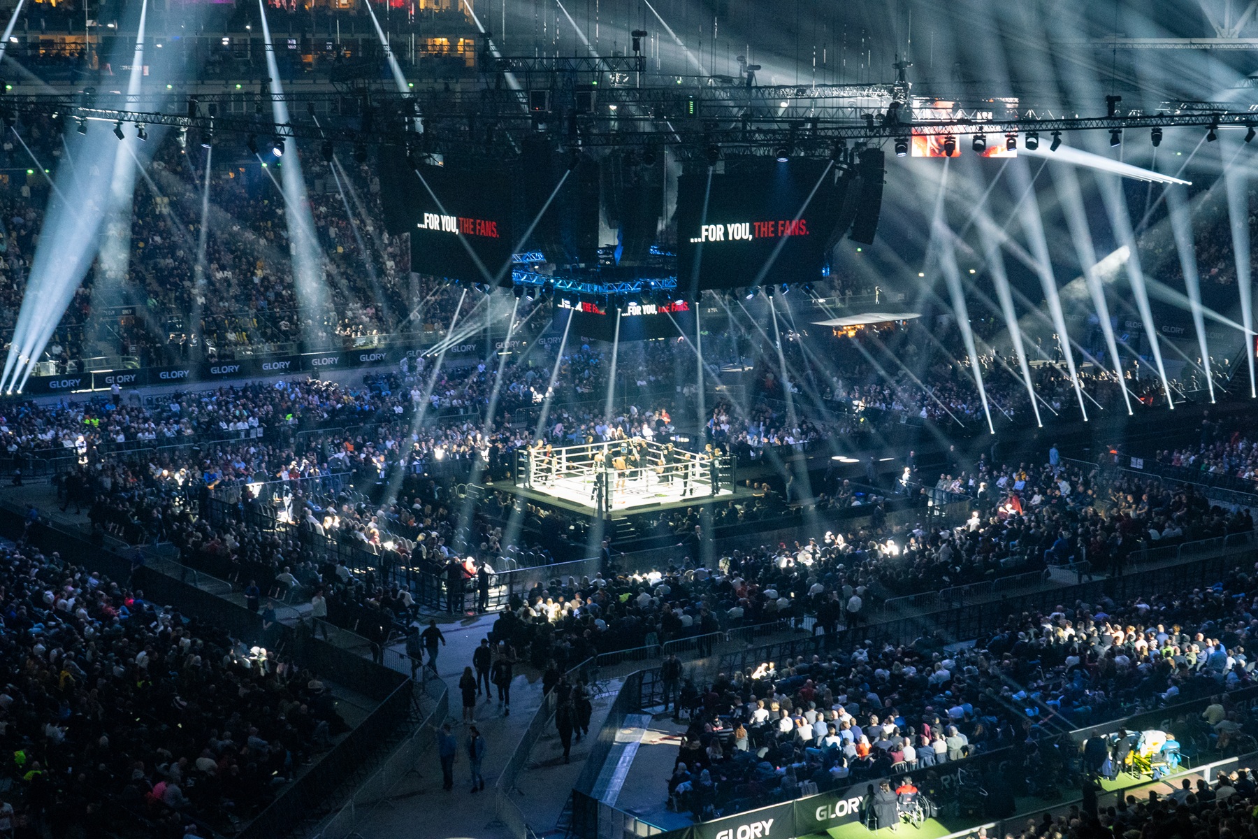 Een sfeervol verlicht stadion met in het midden een ring voor GLORY-gevechten met vechters en scheidsrechters