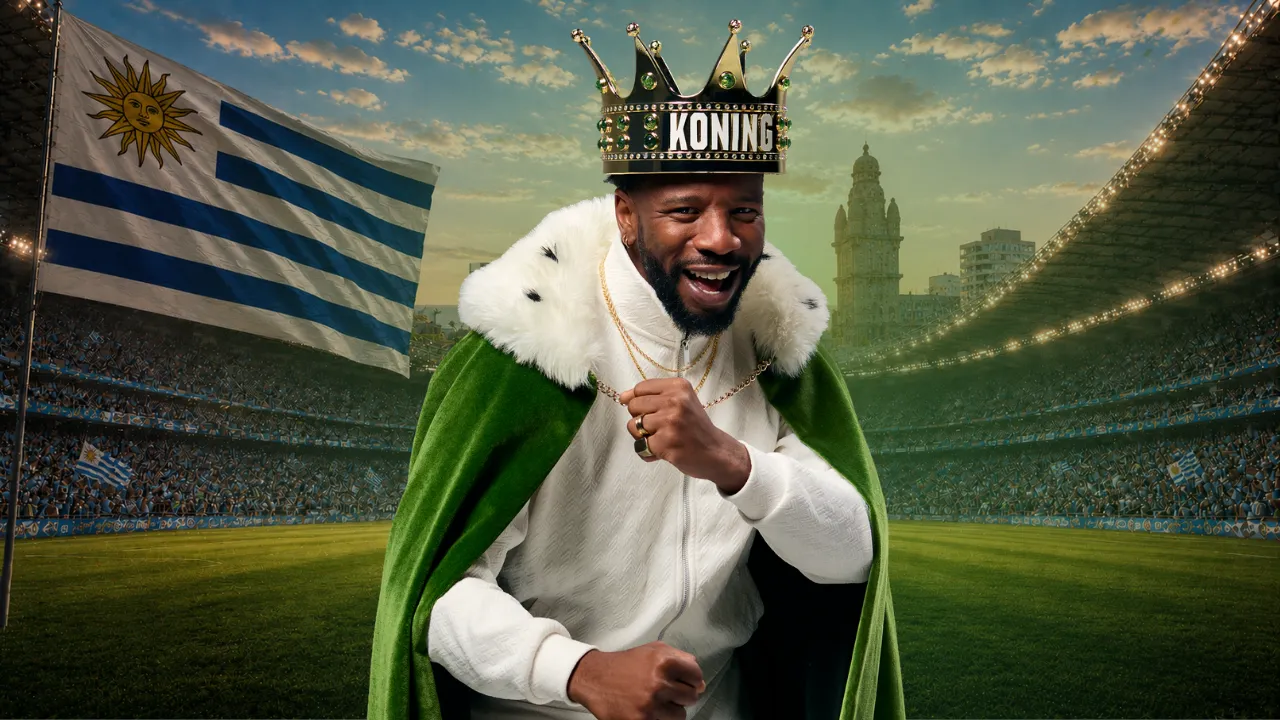 Man met koningskroon en groene cape op een voetbalstadion met Uruguay vlag