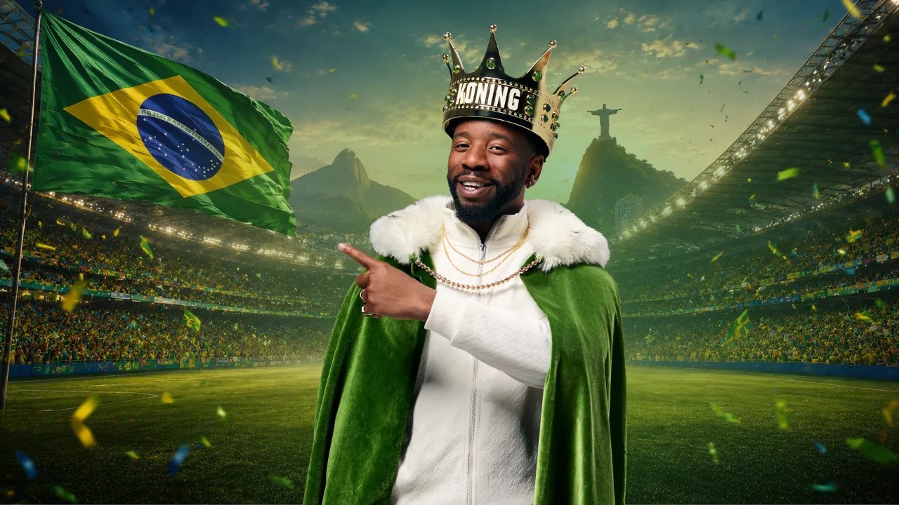 Man met kroon en groene mantel wijst naar vlag van Brazilië op stadion