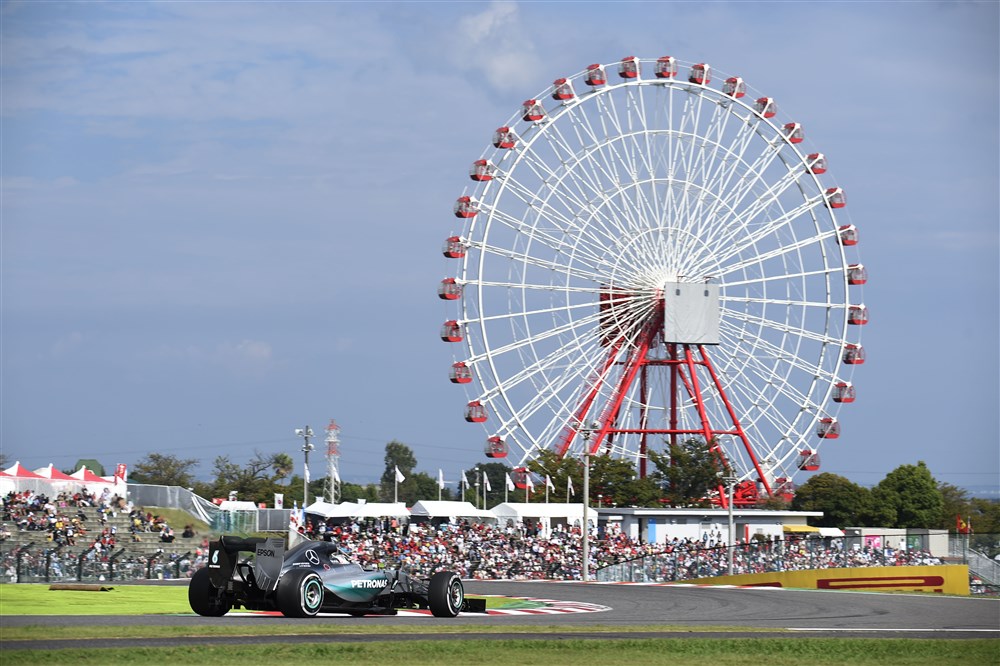 Formule 1 auto rijdt voor een grote reuzenrad en publiek op de tribunes.