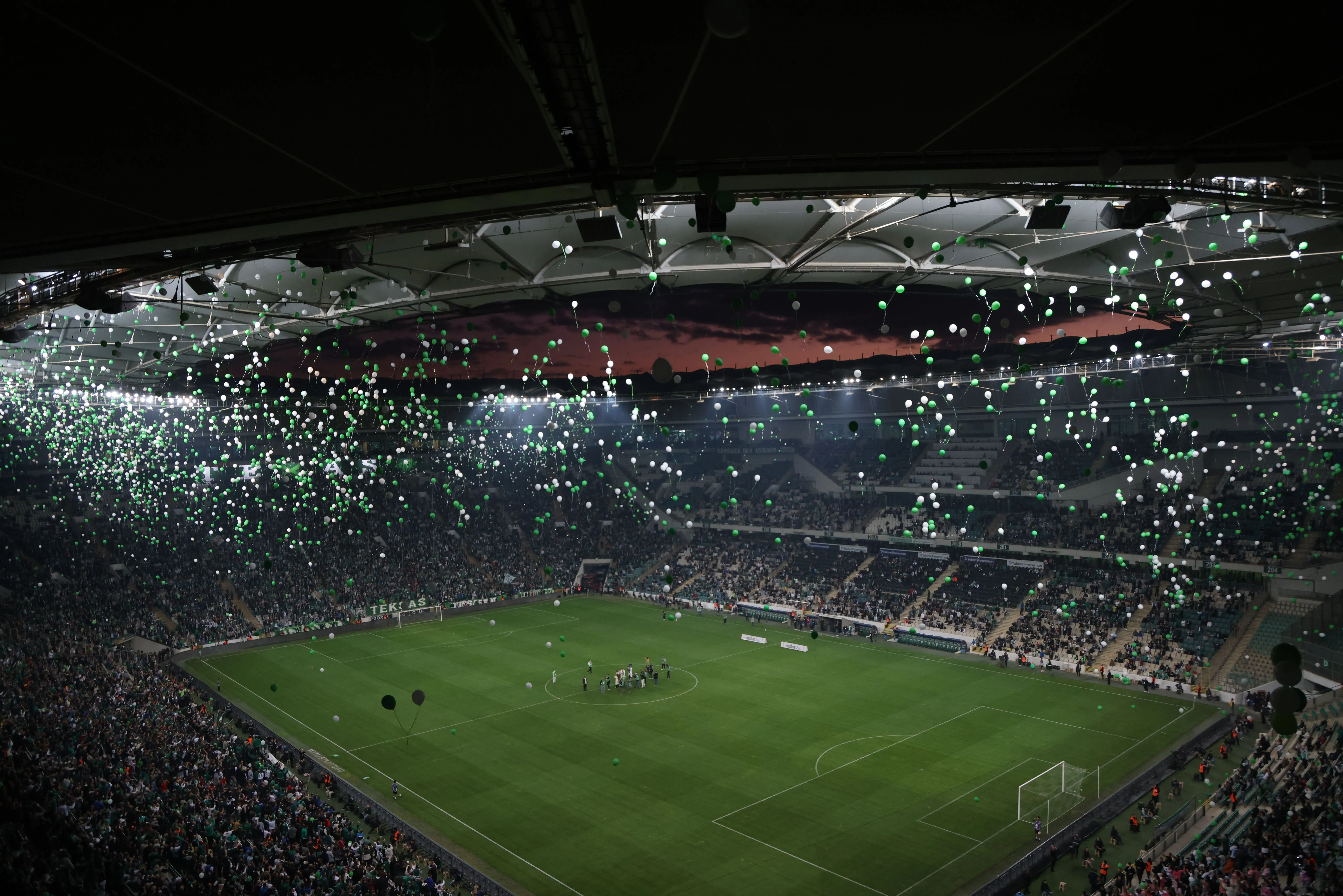 Vol stadion met groene en witte ballonnen tijdens avondwedstrijd