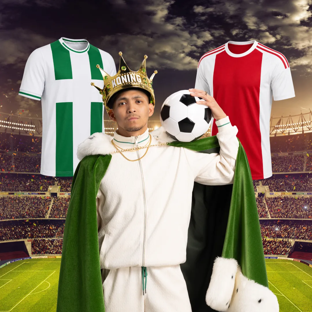 Man met kroon en groene mantel houdt een voetbal vast in stadion met voetbalshirts op de achtergrond