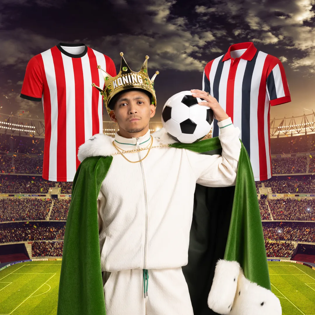 Man met koningskroon en voetbal op schouder in stadion met rood-wit gestreepte sportshirts