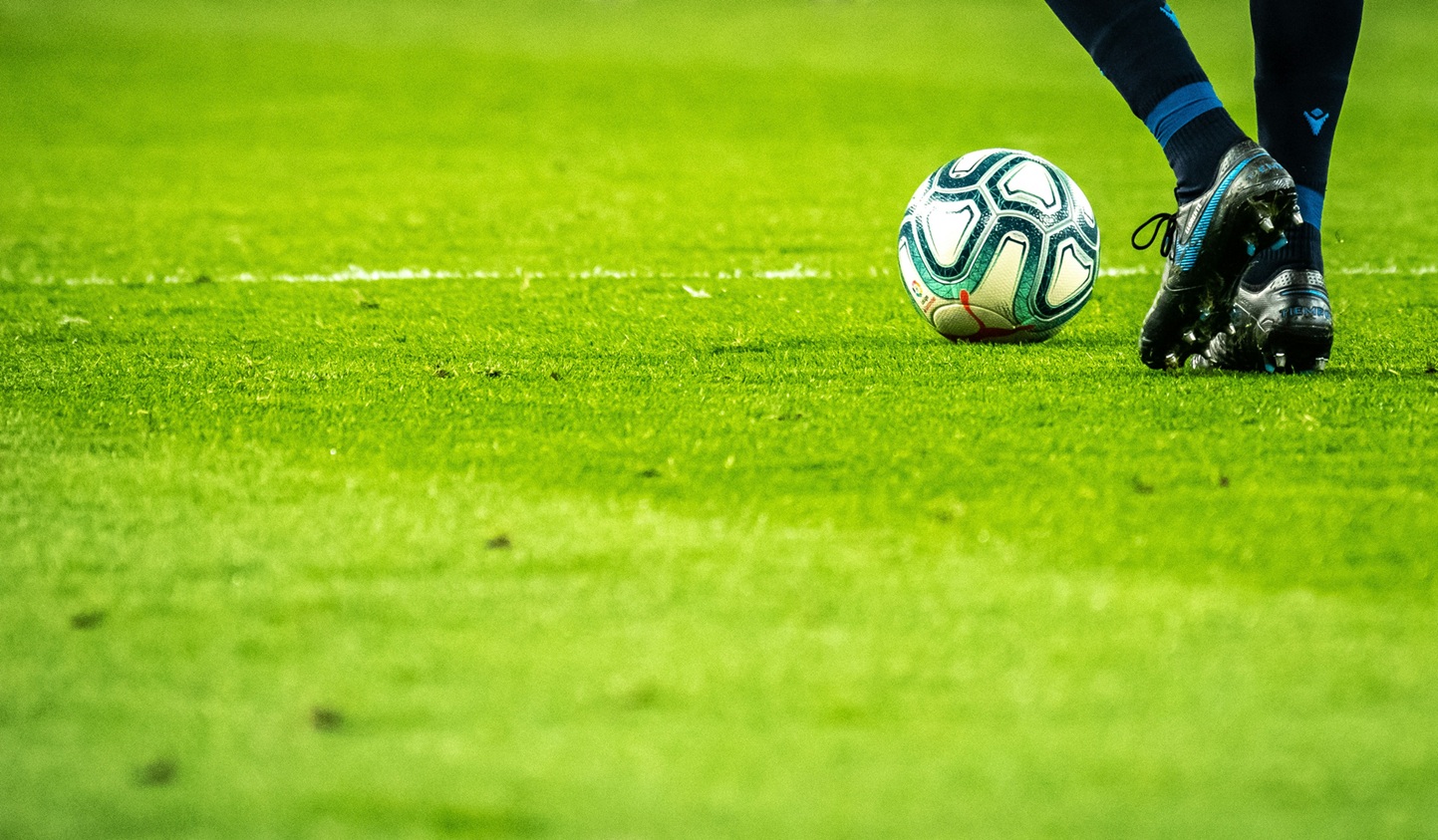 Voetballer met voetbal aan de voet op een veld