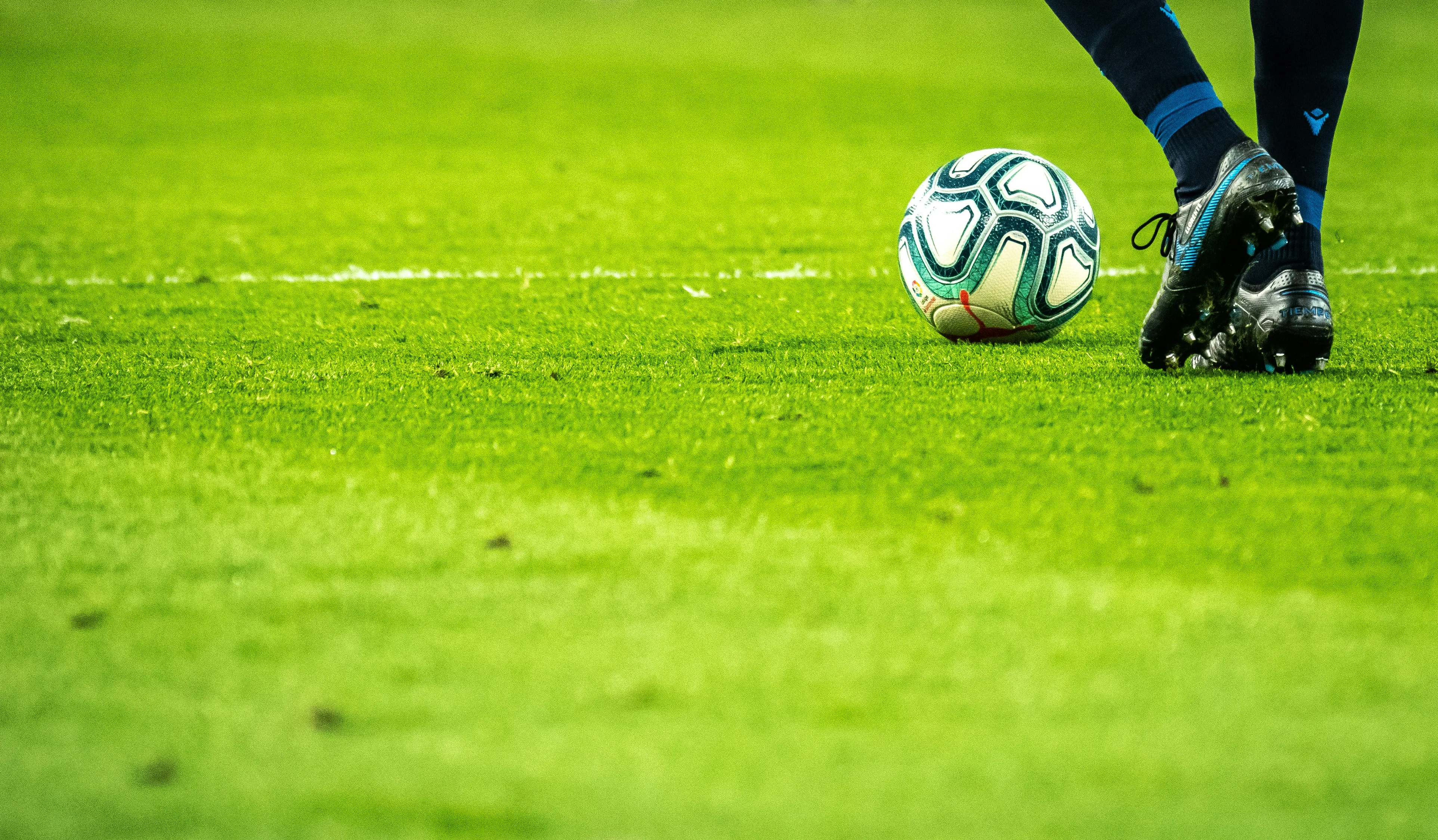 Voetbal op groen grasveld met speler die bal raakt