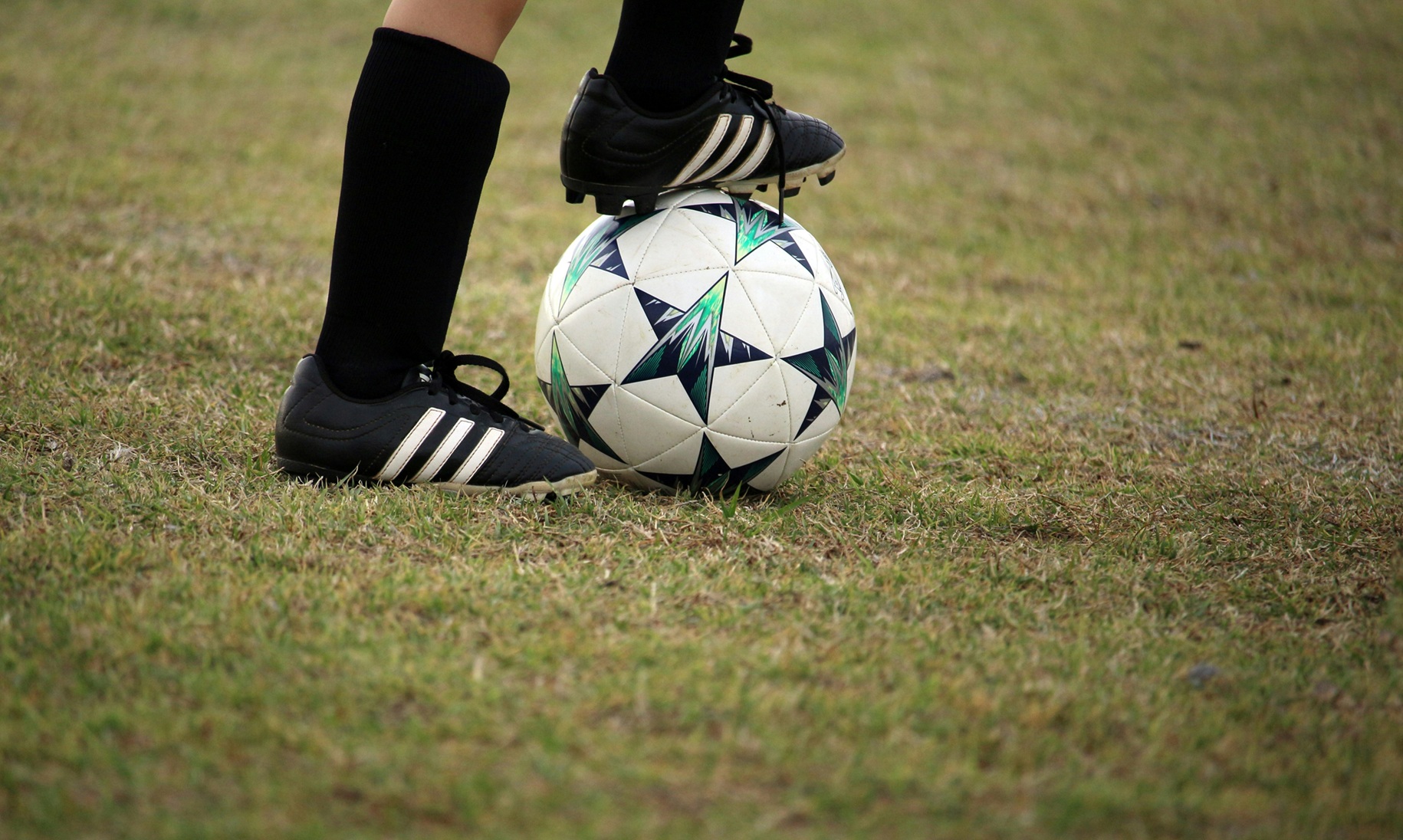 Voetballer met zwarte voetbalschoenen en een bal op het veld.